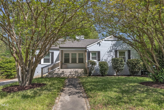 bungalow-style home featuring a front yard, a shingled roof, and brick siding
