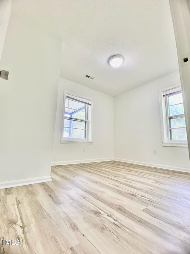 unfurnished room featuring baseboards, a healthy amount of sunlight, visible vents, and light wood-style flooring