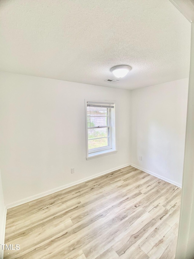 empty room with baseboards, a textured ceiling, visible vents, and light wood-style flooring