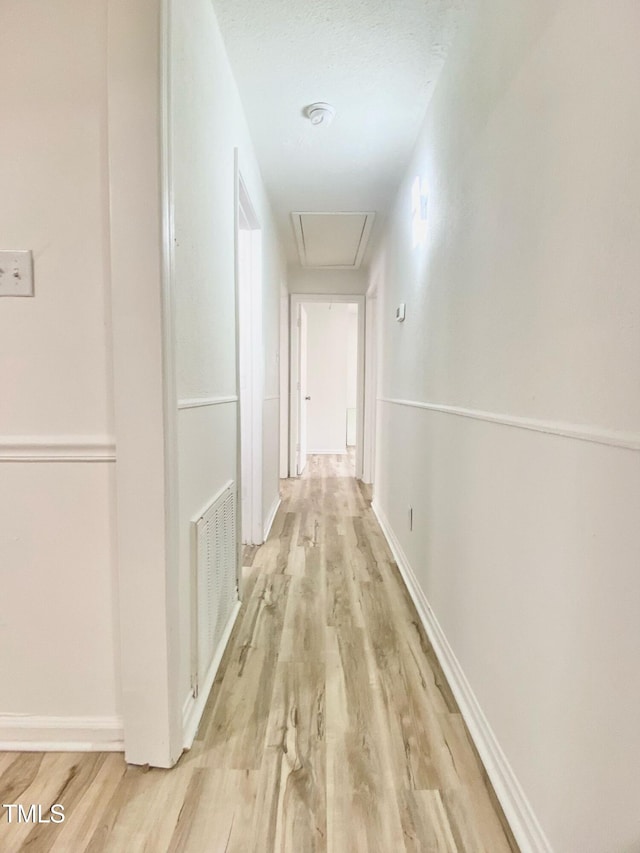 hall with attic access, light wood-style floors, visible vents, and baseboards