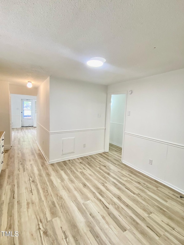spare room with baseboards, a textured ceiling, and light wood-type flooring