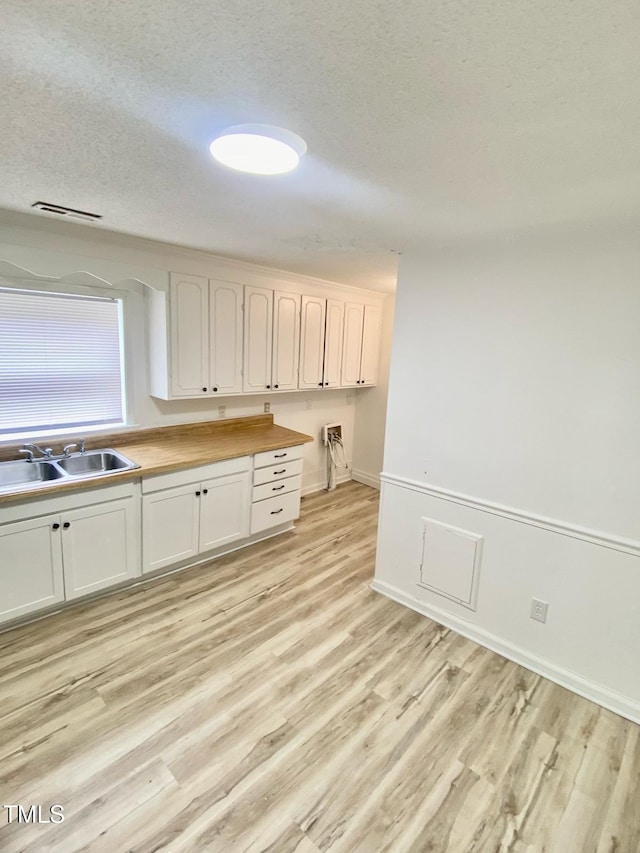 kitchen featuring white cabinets, a sink, a textured ceiling, and light wood-style flooring