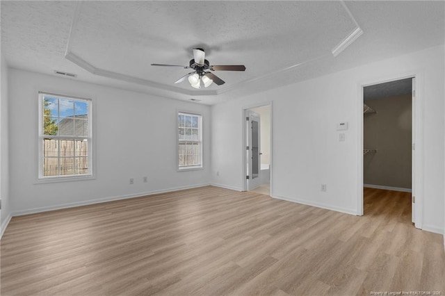 705 Fairfield Cir, Raeford, NC 28376 - unfurnished bedroom with a textured ceiling, light wood-type flooring, a spacious closet, multiple windows, and a tray ceiling