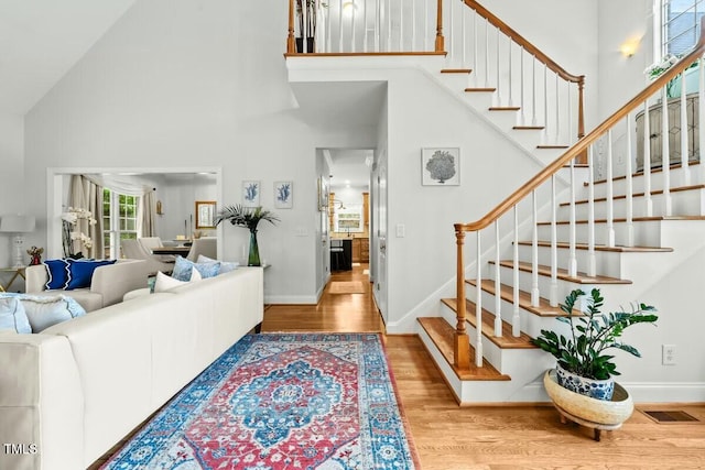 living room featuring wood finished floors, high vaulted ceiling, visible vents, baseboards, and stairs