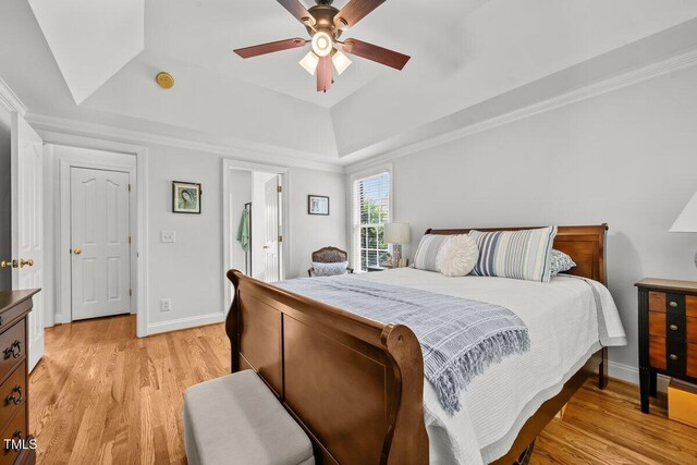 bedroom featuring a tray ceiling, light wood-style flooring, baseboards, and a ceiling fan