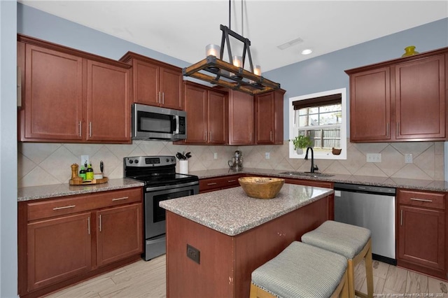 kitchen with appliances with stainless steel finishes, a sink, a center island, light stone counters, and backsplash