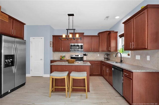 kitchen featuring appliances with stainless steel finishes, a sink, a kitchen island, a kitchen bar, and tasteful backsplash