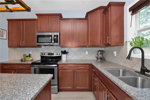 kitchen featuring appliances with stainless steel finishes, a sink, light stone counters, and tasteful backsplash