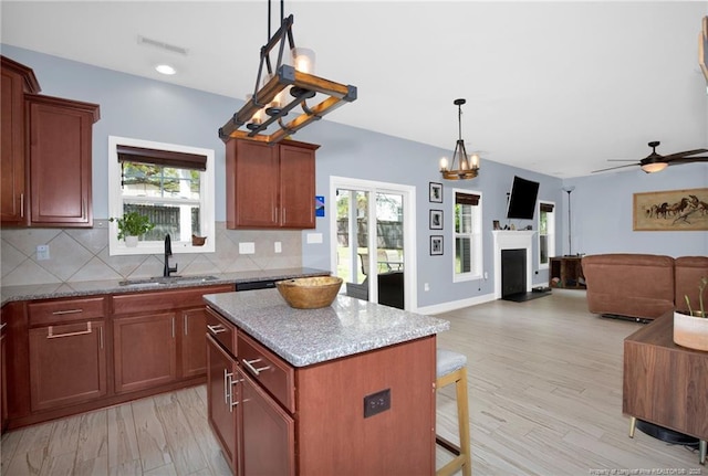 kitchen with a sink, backsplash, a kitchen island, light wood-style flooring, and a fireplace