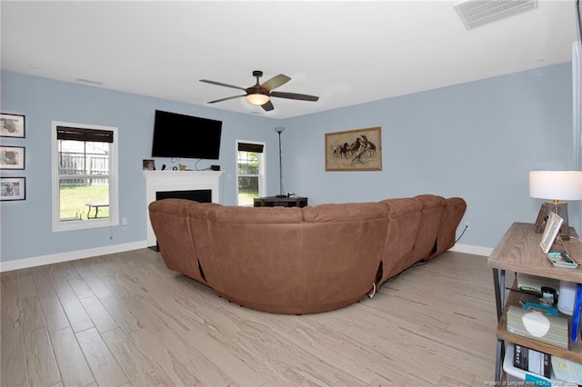living room featuring ceiling fan, a fireplace, light wood-type flooring, and baseboards