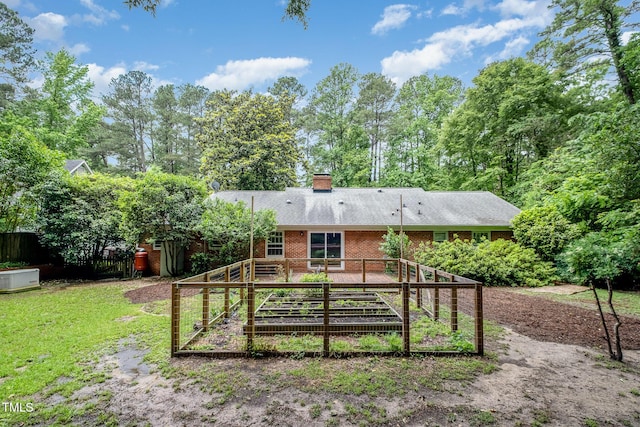 rear view of house featuring a vegetable garden, brick siding, a chimney, and roof with shingles