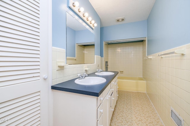 bathroom featuring tile walls, a tub, double vanity, and a wainscoted wall