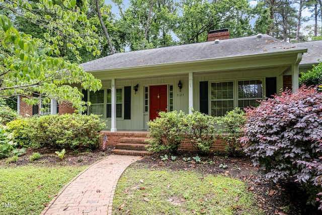 ranch-style home featuring a porch, a chimney, roof with shingles, and brick siding