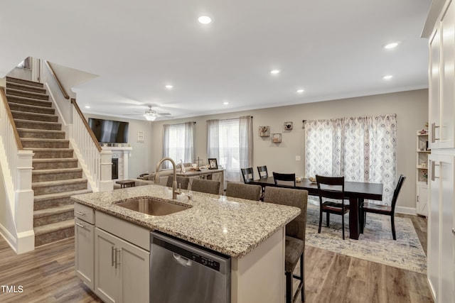 kitchen featuring a fireplace, a kitchen island with sink, ceiling fan, dishwasher, and a sink