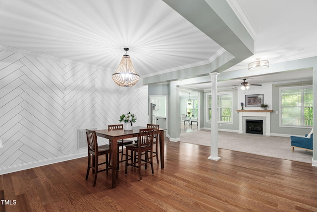 dining space featuring ornamental molding, decorative columns, ceiling fan with notable chandelier, and a fireplace with flush hearth
