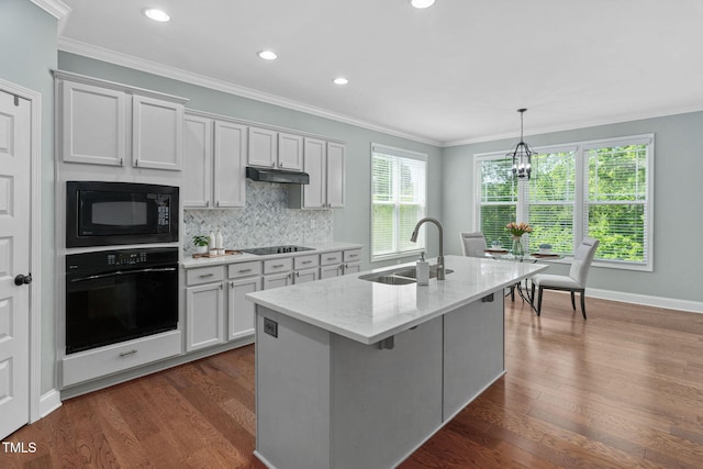 kitchen featuring decorative backsplash, ornamental molding, a kitchen island with sink, a sink, and black appliances