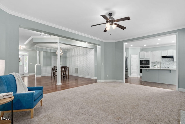 sitting room with decorative columns, a ceiling fan, visible vents, crown molding, and dark carpet