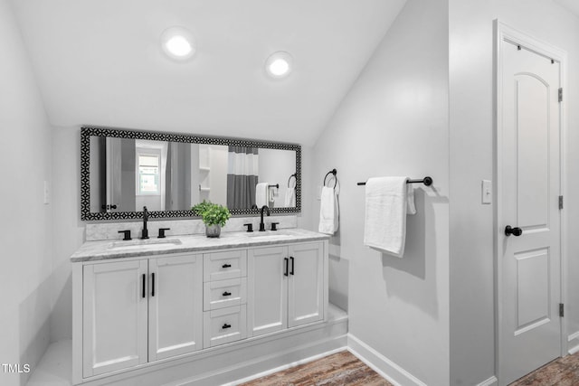 full bathroom with double vanity, baseboards, vaulted ceiling, and a sink