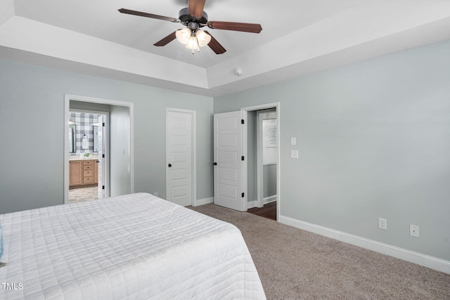 bedroom with carpet floors, baseboards, ceiling fan, a tray ceiling, and ensuite bath