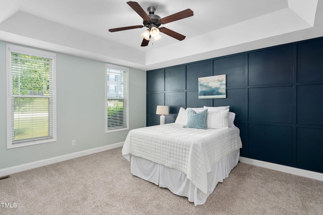 bedroom featuring a ceiling fan, visible vents, a raised ceiling, baseboards, and light carpet