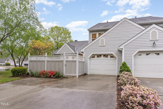 exterior space with driveway, fence, and roof with shingles