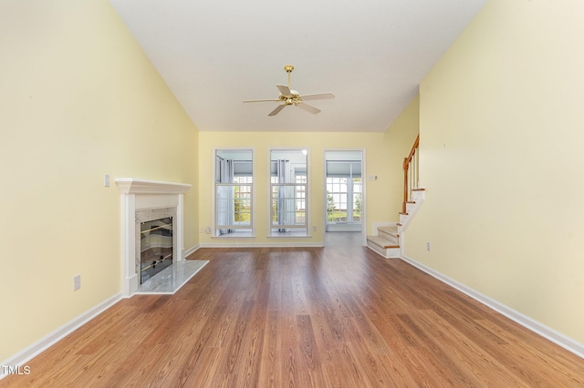 unfurnished living room with stairway, a high end fireplace, wood finished floors, baseboards, and ceiling fan