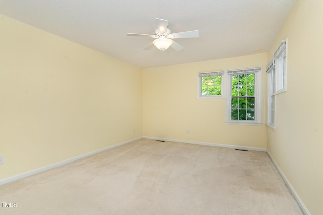 empty room featuring light carpet, a ceiling fan, visible vents, and baseboards