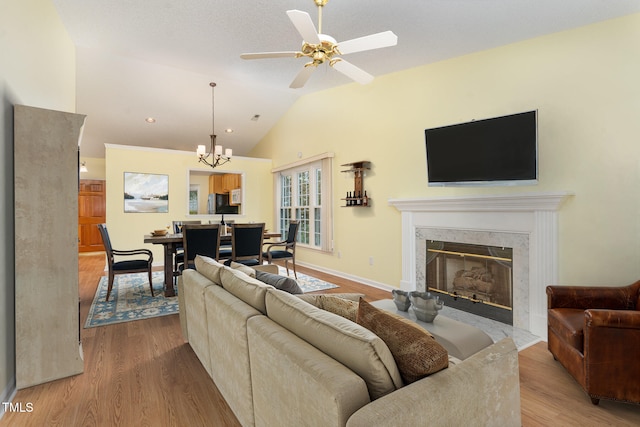 living room with vaulted ceiling, wood finished floors, ceiling fan with notable chandelier, a premium fireplace, and baseboards