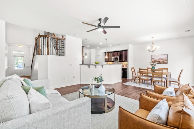 living area featuring dark wood finished floors, ceiling fan with notable chandelier, recessed lighting, baseboards, and stairway