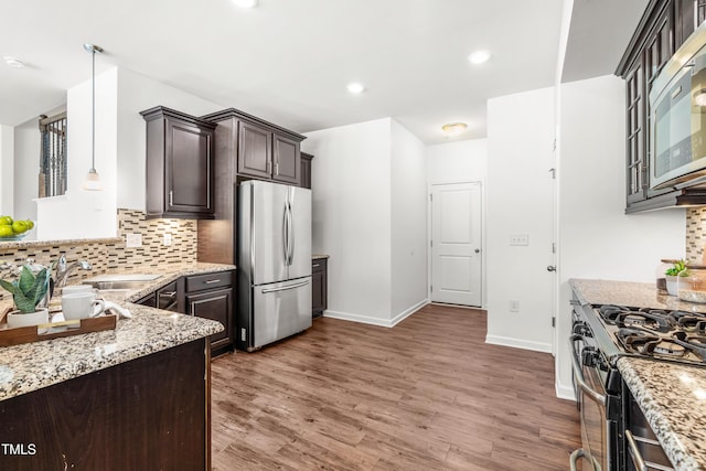 kitchen featuring dark brown cabinetry, appliances with stainless steel finishes, a sink, and light stone countertops