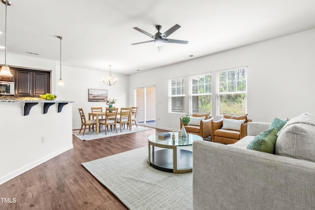 living area featuring baseboards, ceiling fan with notable chandelier, dark wood-style floors, and visible vents