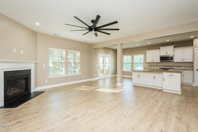 unfurnished living room featuring recessed lighting, light wood finished floors, a ceiling fan, baseboards, and a glass covered fireplace