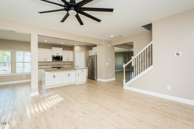 unfurnished living room with light wood-style flooring, baseboards, ceiling fan, and a sink