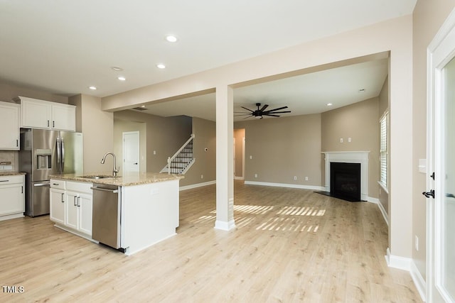 kitchen featuring white cabinets, stainless steel appliances, light wood-style flooring, a sink, and light stone counters