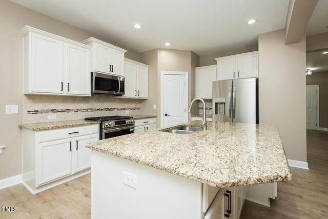 kitchen with white cabinets, light wood-style flooring, a sink, a center island with sink, and appliances with stainless steel finishes