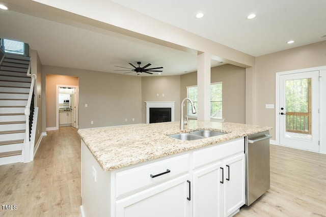 kitchen featuring stainless steel dishwasher, a sink, light stone countertops, a kitchen island with sink, and ceiling fan