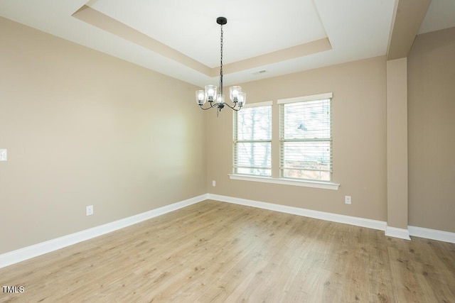 spare room featuring light wood-style flooring, baseboards, an inviting chandelier, and a raised ceiling