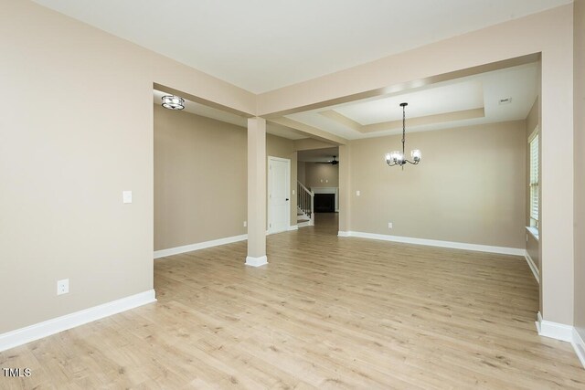 interior space featuring a tray ceiling, light wood-style flooring, baseboards, and a notable chandelier
