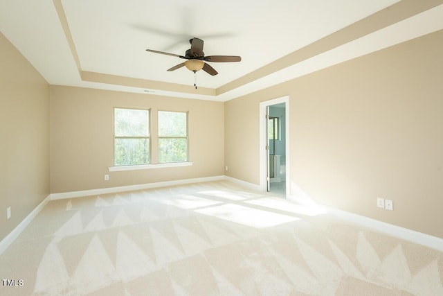 spare room featuring baseboards, light carpet, a ceiling fan, and a raised ceiling