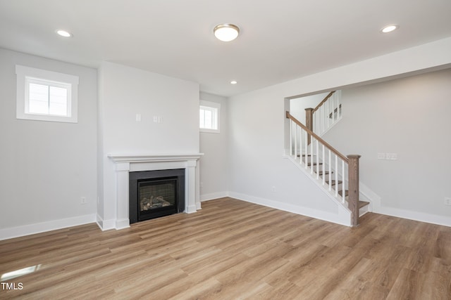unfurnished living room with light wood-type flooring, a glass covered fireplace, recessed lighting, stairway, and baseboards