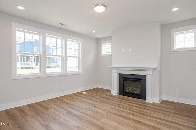 unfurnished living room with visible vents, light wood-style flooring, plenty of natural light, and a glass covered fireplace