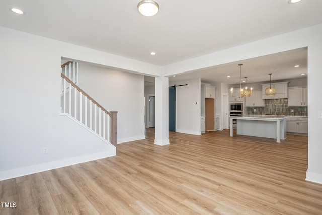 unfurnished living room with baseboards, a barn door, light wood-type flooring, stairway, and recessed lighting