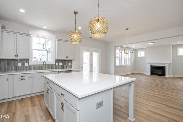 kitchen with light wood-style floors, a kitchen island, light countertops, a sink, and decorative backsplash