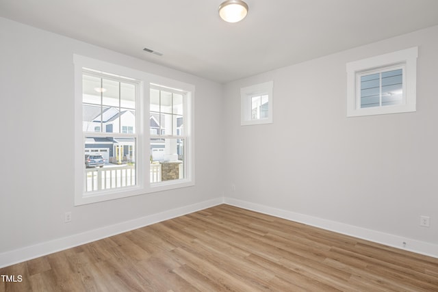 empty room with light wood finished floors, visible vents, and baseboards
