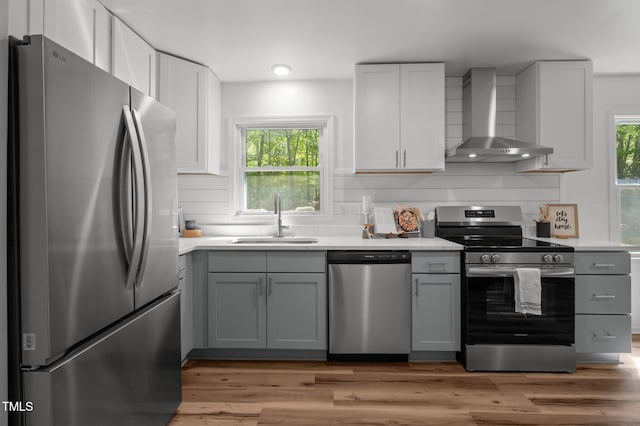 kitchen featuring wall chimney range hood, a wealth of natural light, appliances with stainless steel finishes, and a sink