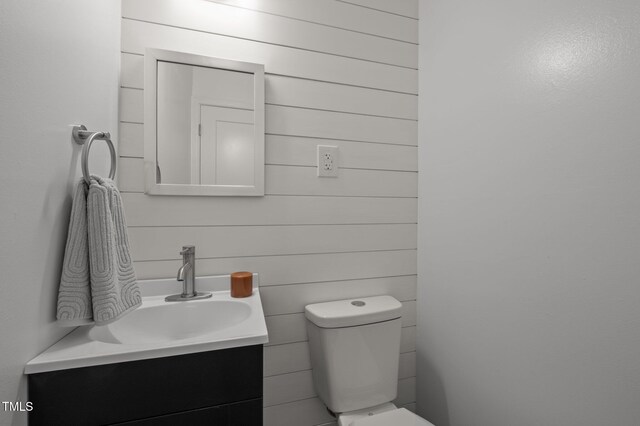 bathroom with toilet, vanity, and wooden walls