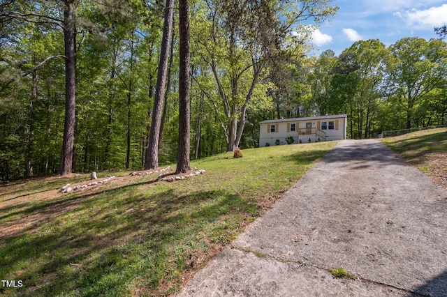 manufactured / mobile home with fence, a front lawn, driveway, and a forest view