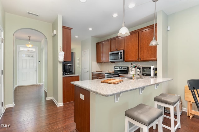 kitchen featuring brown cabinetry, a peninsula, appliances with stainless steel finishes, and a sink