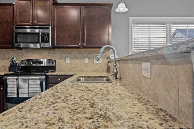 kitchen with a sink, dark brown cabinets, light stone countertops, decorative backsplash, and stainless steel appliances