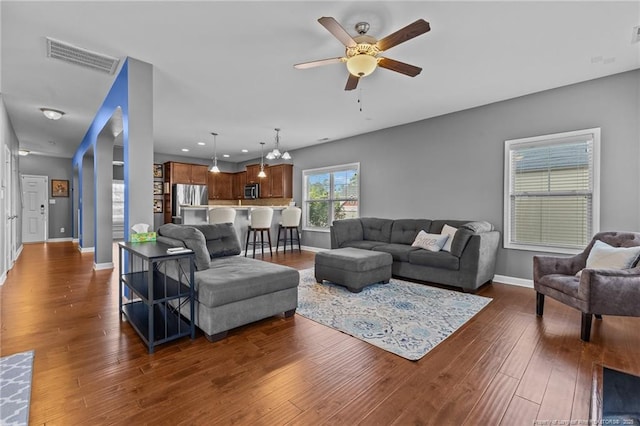 living room with dark wood-type flooring, visible vents, ceiling fan, and baseboards